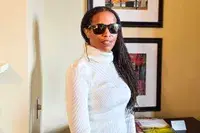 A person wearing Ray-Ban Chromance Sunglasses and a white turtleneck, standing indoors near framed pictures on a wall