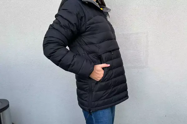 A person facing to the side with their hands in their pockets while wearing the Fjallraven Expedition Pack Down Anorak in front of a white wall