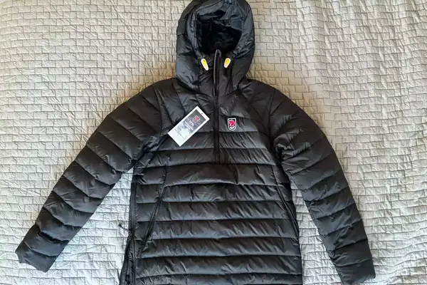 The Fjallraven Expedition Pack Down Anorak with tags on a fabric background