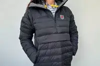 A person wearing the Fjallraven Expedition Pack Down Anorak in front of a white wall with their hands in their pockets