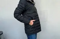 A person facing to the side with their hands in their pockets while wearing the Fjallraven Expedition Pack Down Anorak in front of a white wall