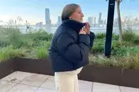 A person zipping up the Canada Goose Garnet Cropped Puffer in front of a city skyline