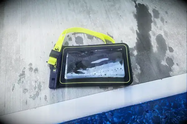 A wet Case-Mate Pelican Marine IP68 Waterproof Phone Pouch containing a phone on concrete near water