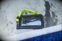 A wet Case-Mate Pelican Marine IP68 Waterproof Phone Pouch containing a phone on concrete near water