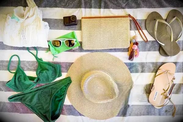Various vacation accessories arranged on a striped surface, including a bikini, hat, camera, sunglasses, and flip-flops