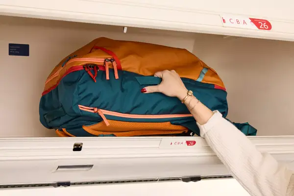 A person places the Cotopaxi Allpa 42L Travel Pack into an overhead compartment