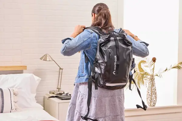 A person adjusts the straps on the Earth Pak Summit Dry Bag Backpack