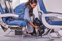 A person places the Earth Pak Summit Dry Bag Backpack under the seat in front of them