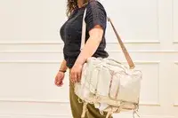 A person wears the Calpak Terra 26L Laptop Duffel Backpack by the strap
