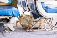 A person places a Calpak Terra 26L Laptop Duffel Backpack under the seat in front of them