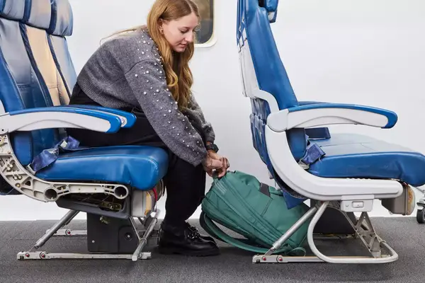 A person placing the Samsonite Elevation Plus Backpack under an airplane seat