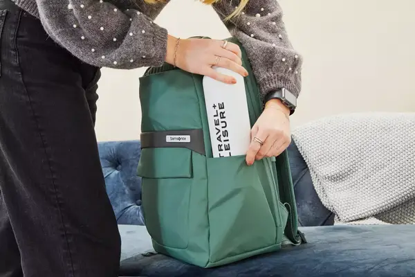 Hands placing a water bottle in the side pouch of the Samsonite Elevation Plus Backpack 