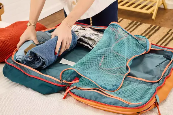 A person packs clothing into the Cotopaxi Allpa 42L Travel Pack