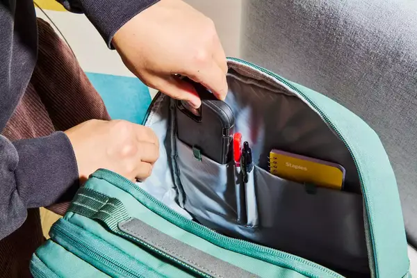 Hands placing a phone inside of the Samsonite Elevation Plus Backpack