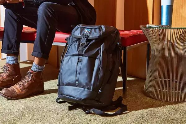 Kühl Eskape 25 Backpack displayed on carpet next to red bench with person seated on it