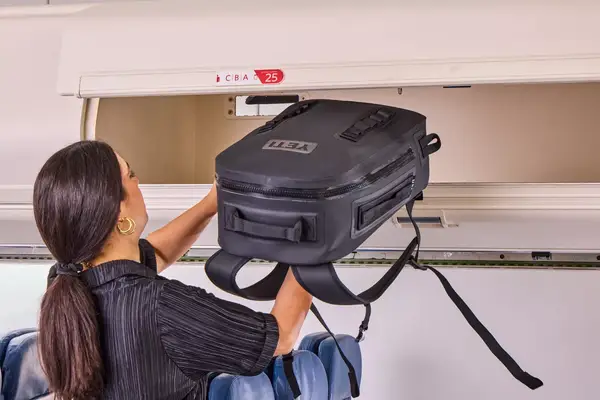 A person places the Yeti Panga 28L Waterproof Backpack into an overhead compartment
