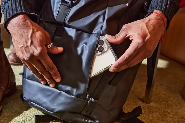 Hands inserting a smart phone inside the front pocket of the Kühl Eskape 25 Backpack