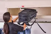 A person places the Yeti Panga 28L Waterproof Backpack into an overhead compartment