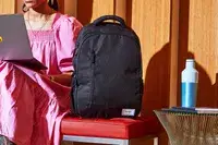 Person sitting next to the Solo Re:Define Backpack on a red leather bench