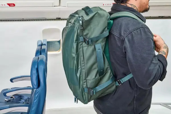 A person wears the Away The Outdoor Convertible Backpack 45L next to airplane seats