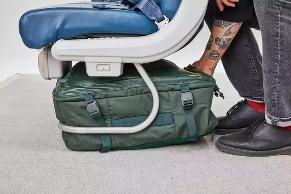 Hand places the Away The Outdoor Convertible Backpack 45L under a seat