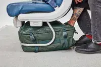 Hand places the Away The Outdoor Convertible Backpack 45L under a seat