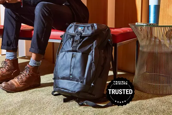 A Kuhl backpack sits on the ground next to a person