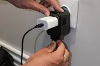 Two hands holding the EPICKA Universal Travel Adapter plugged into the wall