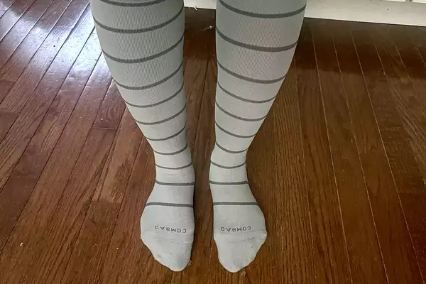 Comrad Knee High Compression Socks On Persons Feet Standing On Hardwood Floor