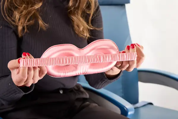 A person stretching the strap on the Slip Lovely Lashes Contour Sleep Mask in an airplane