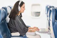 A person using a laptop on a plane while wearing the Bowers & Wilkins Px7 S2e 