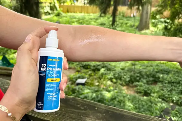 A hand spraying Sawyer Picaridin Insect Repellent on an arm outside