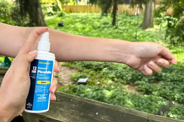 A person spraying Sawyer Picaridin Insect Repellent on an arm outside