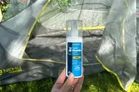 A hand holding the Sawyer Picaridin Insect Repellent in front of a camping tent