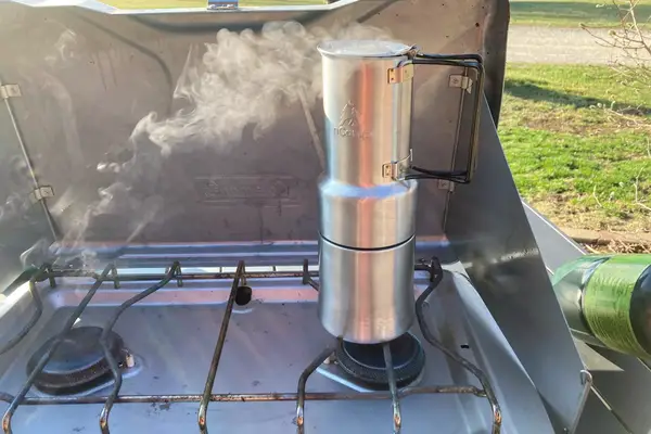The nCamp CafÃ© Portable Coffee Maker on a camp stove with steam coming out of the top