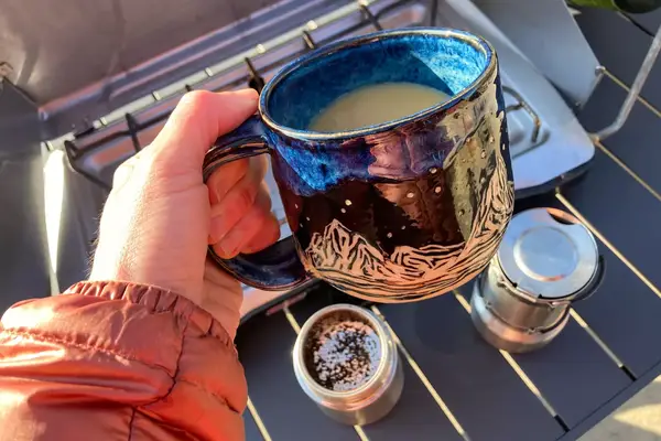 A person holds up a mug of coffee brewed in the nCamp CafÃ© Portable Coffee Maker