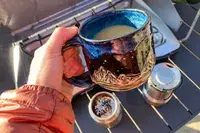 A person holds up a mug of coffee brewed in the nCamp CafÃ© Portable Coffee Maker