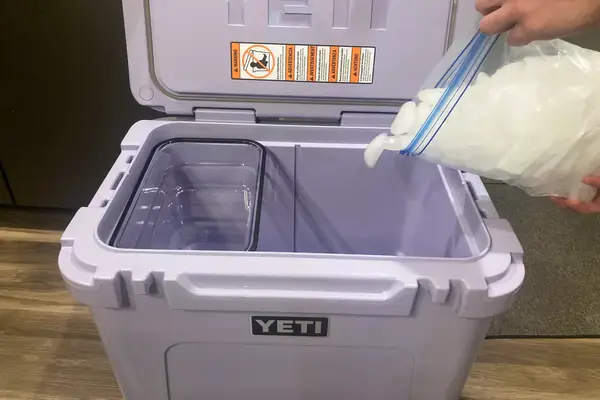 A person adding ice to Yeti Roadie 60 Wheeled Cooler