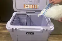 A person adding ice to Yeti Roadie 60 Wheeled Cooler
