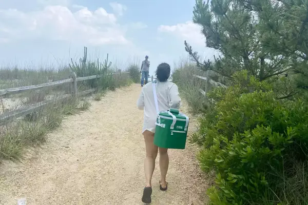 A person carries the RTIC Insulated Soft Cooler Bag on her shoulder while walking on a beach trail