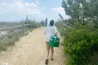 A person carries the RTIC Insulated Soft Cooler Bag on her shoulder while walking on a beach trail