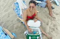 A person on a beach removes a canned beverage from the RTIC Insulated Soft Cooler Bag