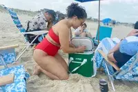 A person on a beach removes a canned beverage from the RTIC Insulated Soft Cooler Bag
