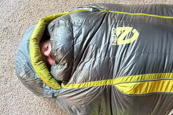 A person peeks out of the Nemo Coda Genderless Endless Promise Down Mummy Sleeping Bag