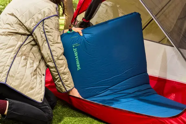A person places the fully inflated Therm-a-Rest BaseCamp Sleeping Pad into a tent
