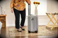 A person rolls the Monos Expandable Carry-on Pro over a rug