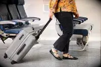 A person rolls the Monos Expandable Carry-on Pro over carpet
