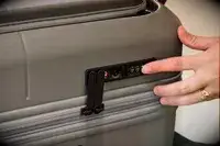 A person presses the lock on the side of the Monos Expandable Carry-on Pro