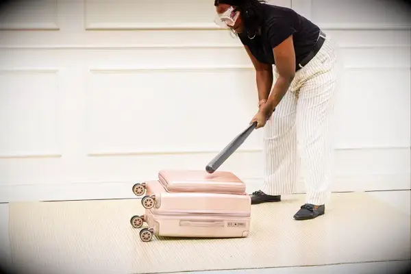 A person hits the Calpak Ambeur Carry-On with a baseball bat