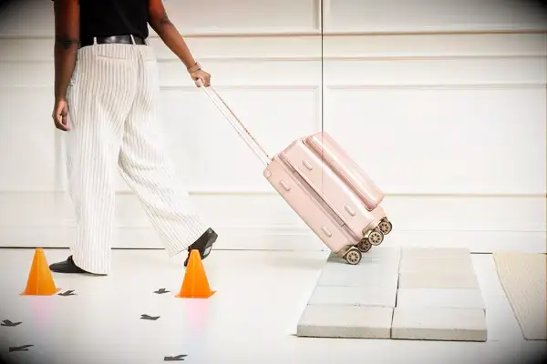 A person wheels the Calpak Ambeur Carry-On across the floor